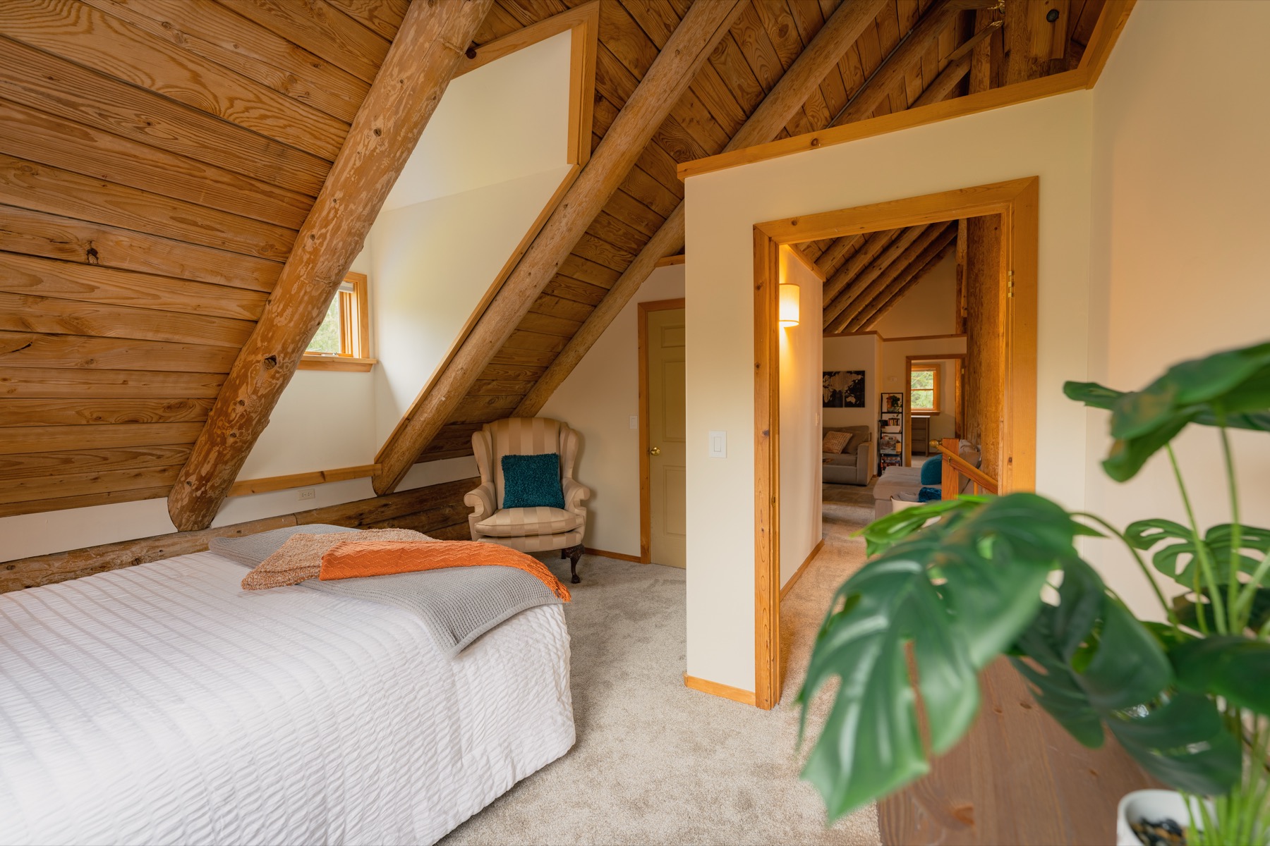 Loft bedroom with exposed beams, soft carpet, and a reading chair